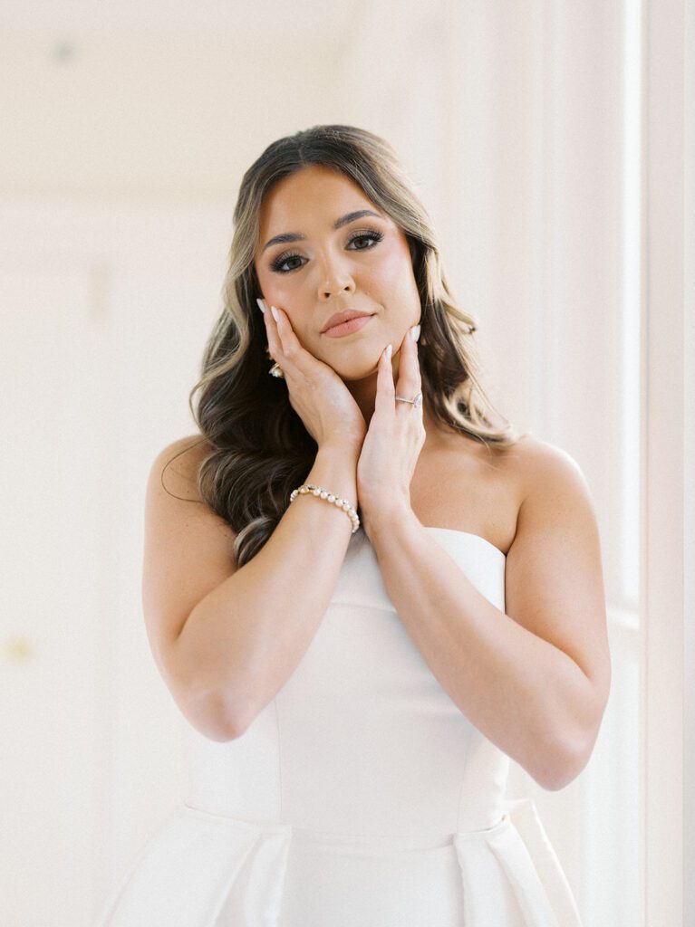 Soft bridal portrait of Grace framing her face with both hands, showing her diamond engagement ring and pearl bracelet in a strapless white ballgown at McAlister-Leftwich Greensboro NC — Raleigh wedding photographer